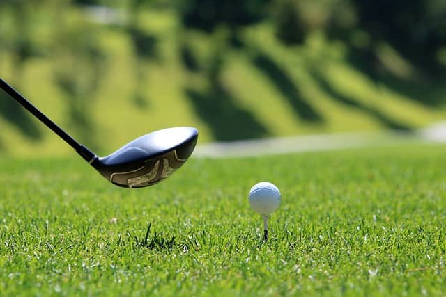 Closeup of a golf club and a golf ball on a tee.